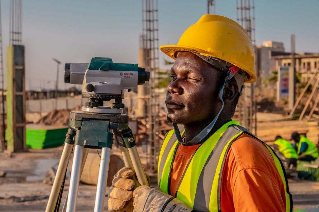 pexels-photo-30379883 A construction worker using a theodolite for land surveying at a building site.